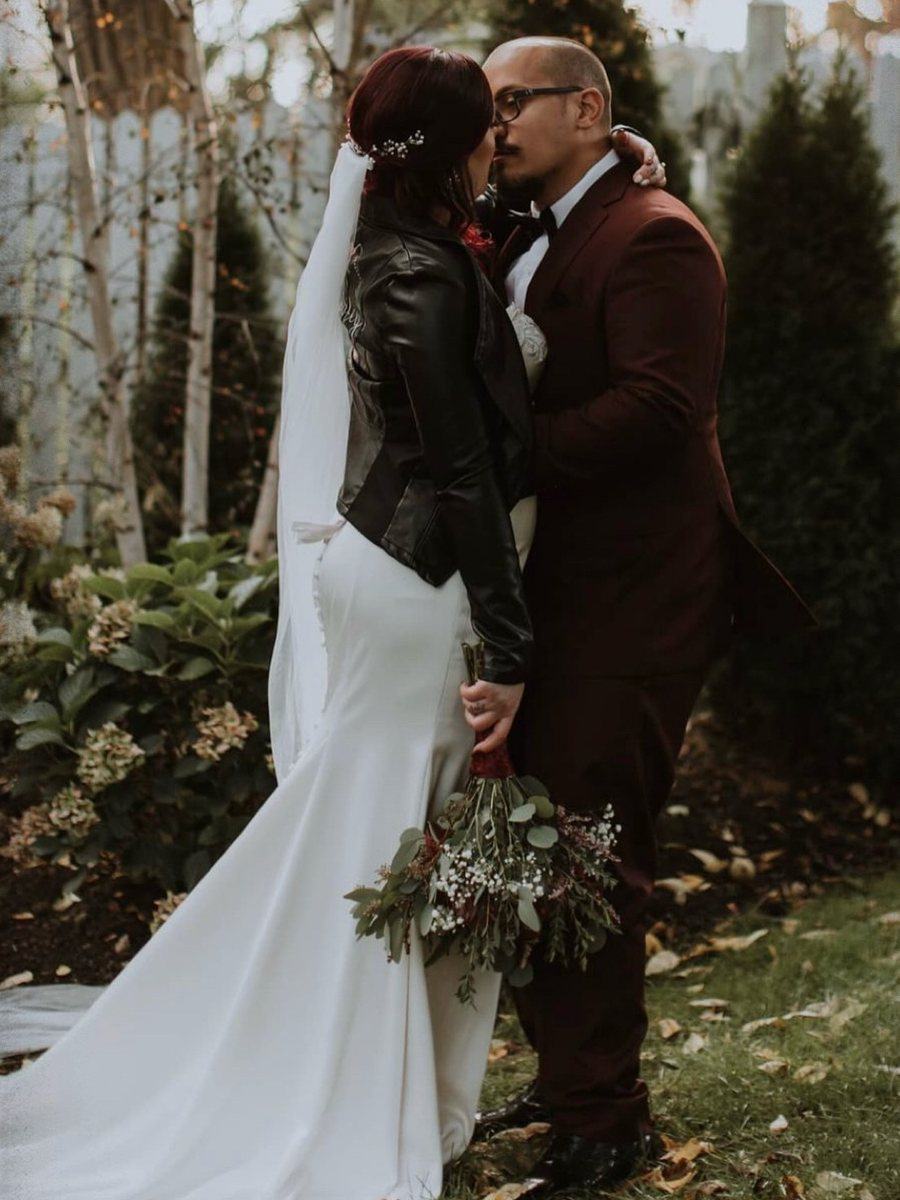 Bride in a veil and leather jacket kissing her groom outdoors in autumn