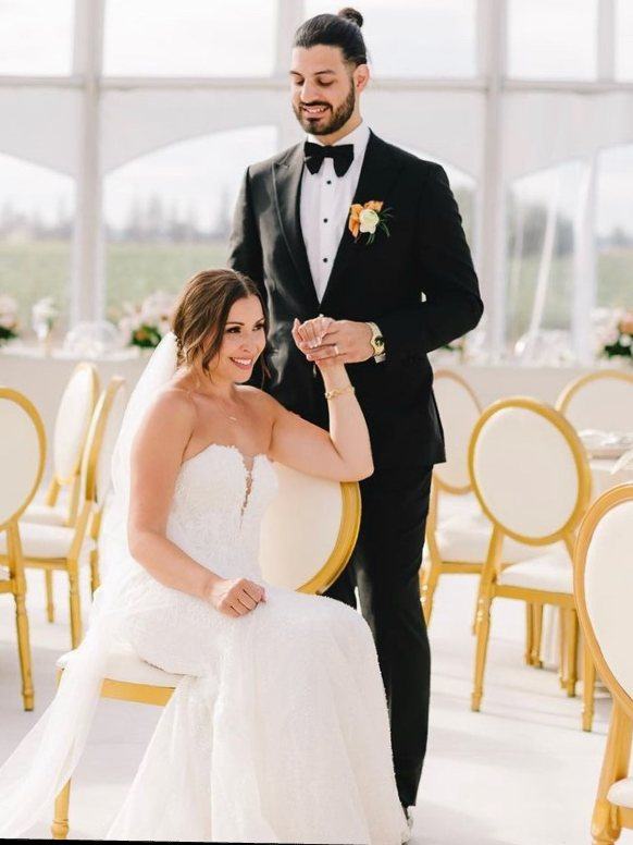 Bride seated among gold chairs holding her groom’s hand