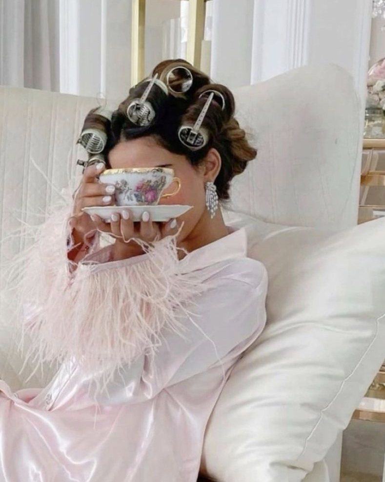 Woman in hair rollers and a feathered satin robe sipping from a teacup